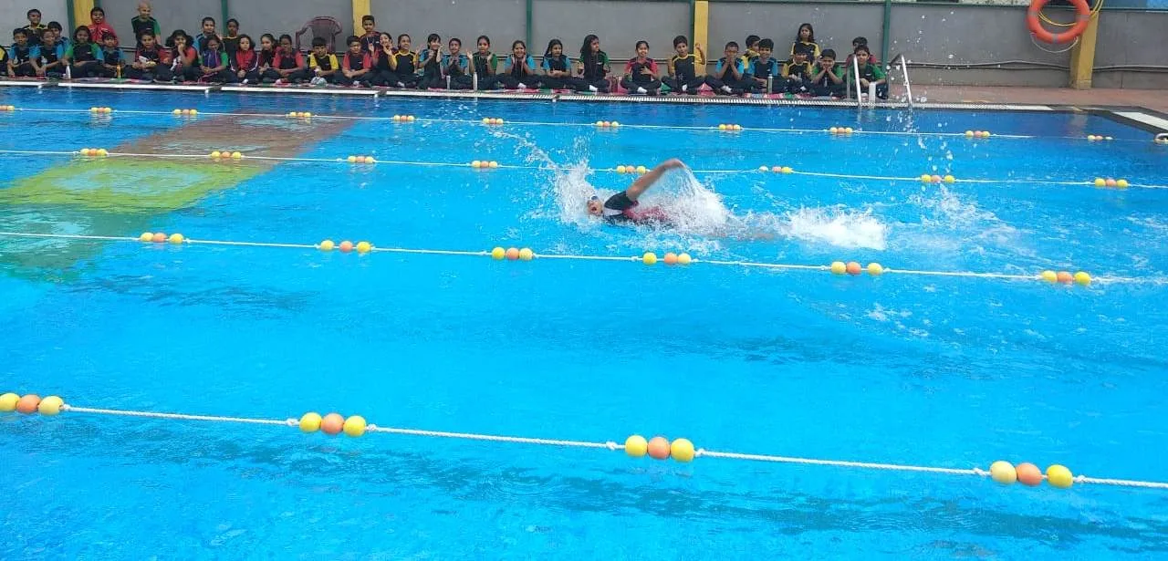 A GoldenBee student swimming during an inter-house gala as classmates watch
